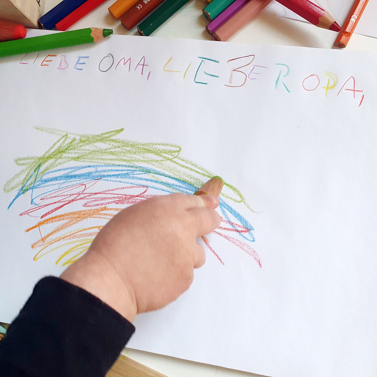 Kinderhand mit Buntstift malt einen Regenbogen.